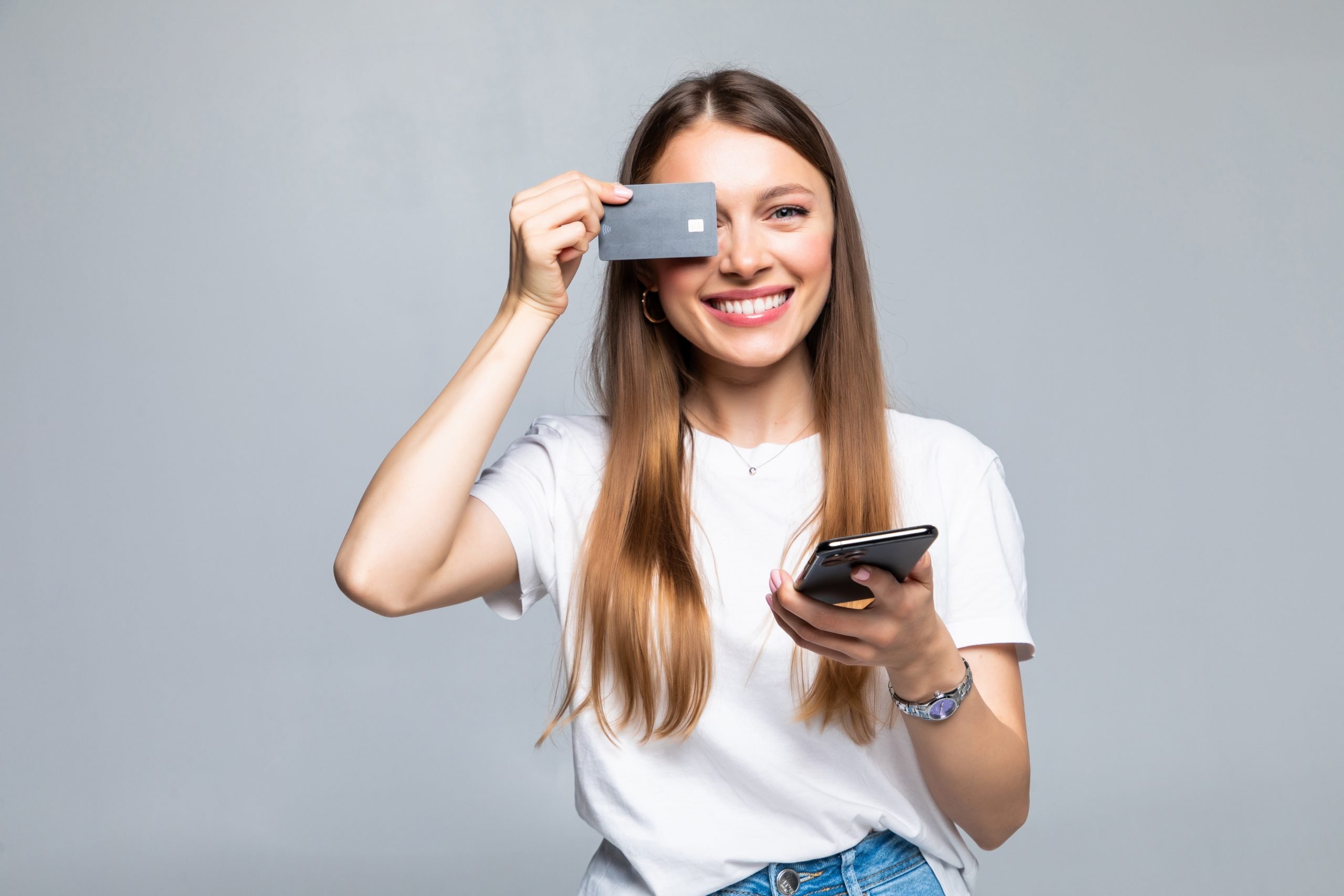 Cheerful excited young woman with mobile phone and credit card over white background