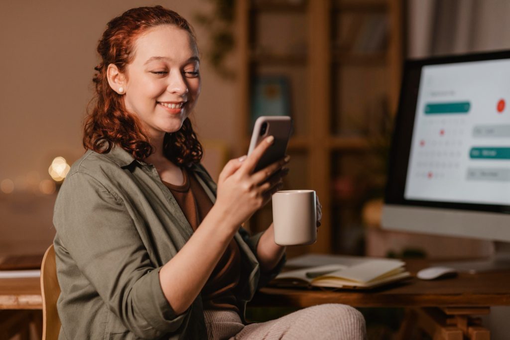 woman-home-using-smartphone-front-computer-while-having-coffee