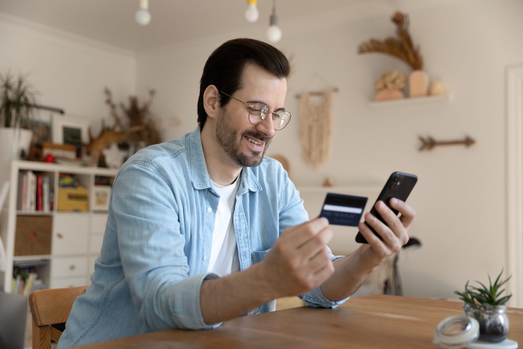 Millennial man using card and phone to provide payment online