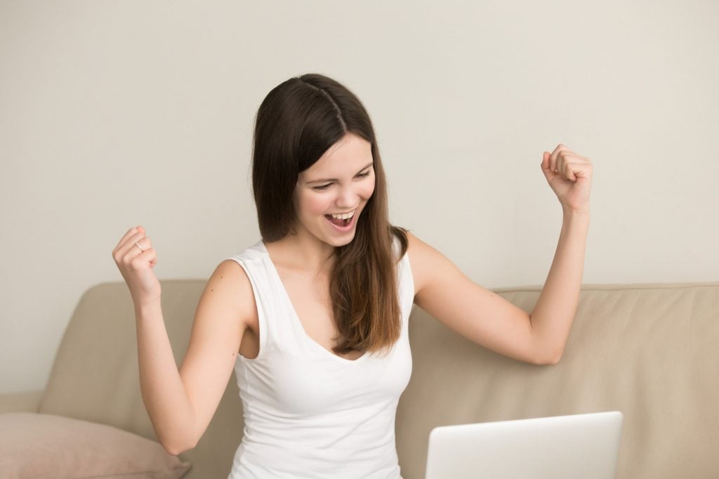 excited woman celebrates looking at laptop