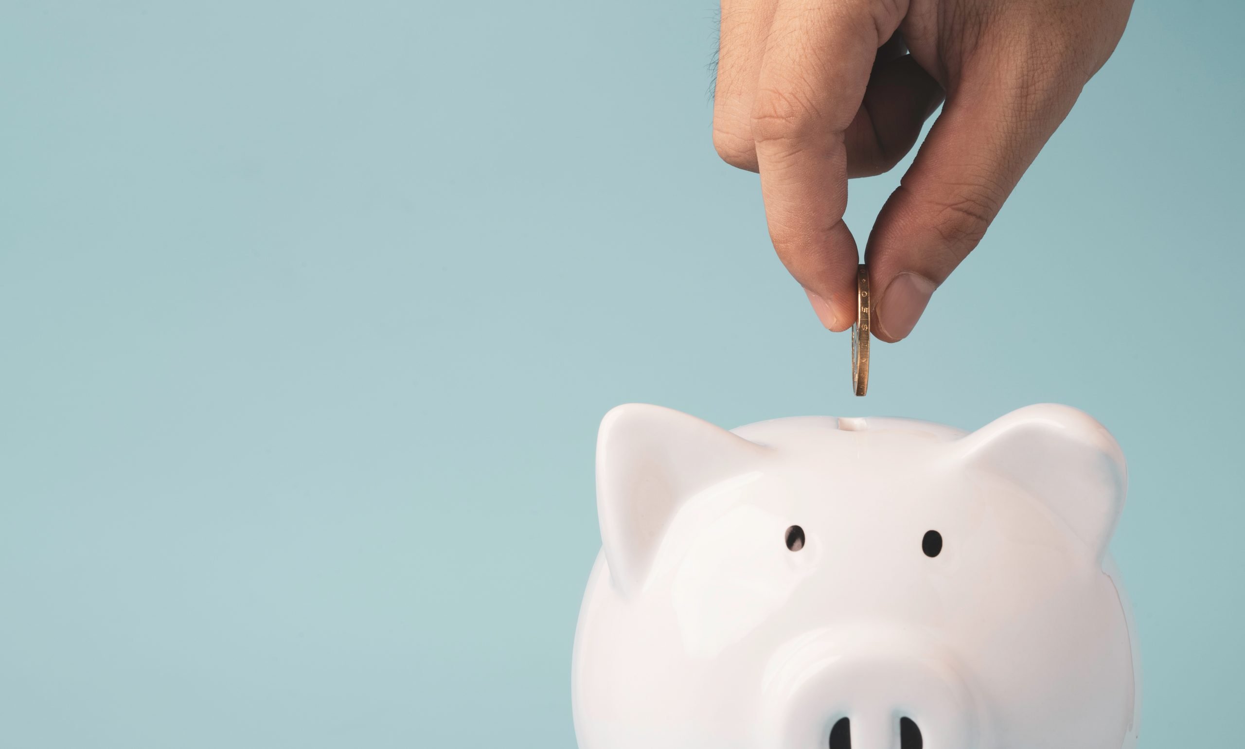 Hand putting coin to white piggy bank saving on blue background