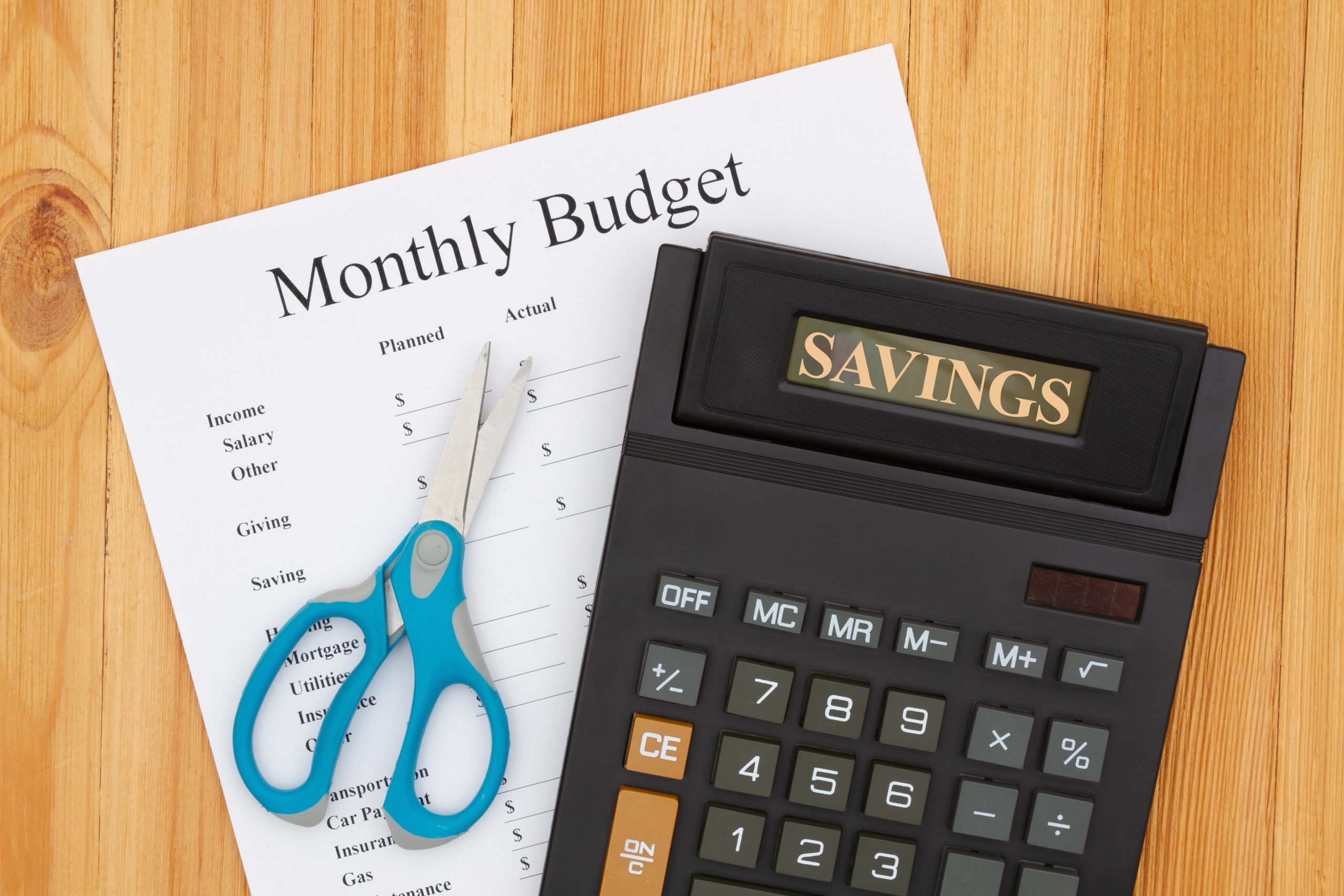 Cutting your monthly budget with a calculator with a display and scissors on wooden desk