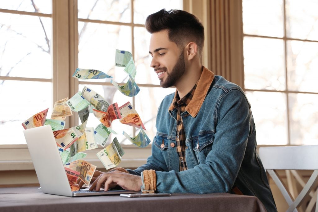 Man with modern laptop and flying euro banknotes at table indoor