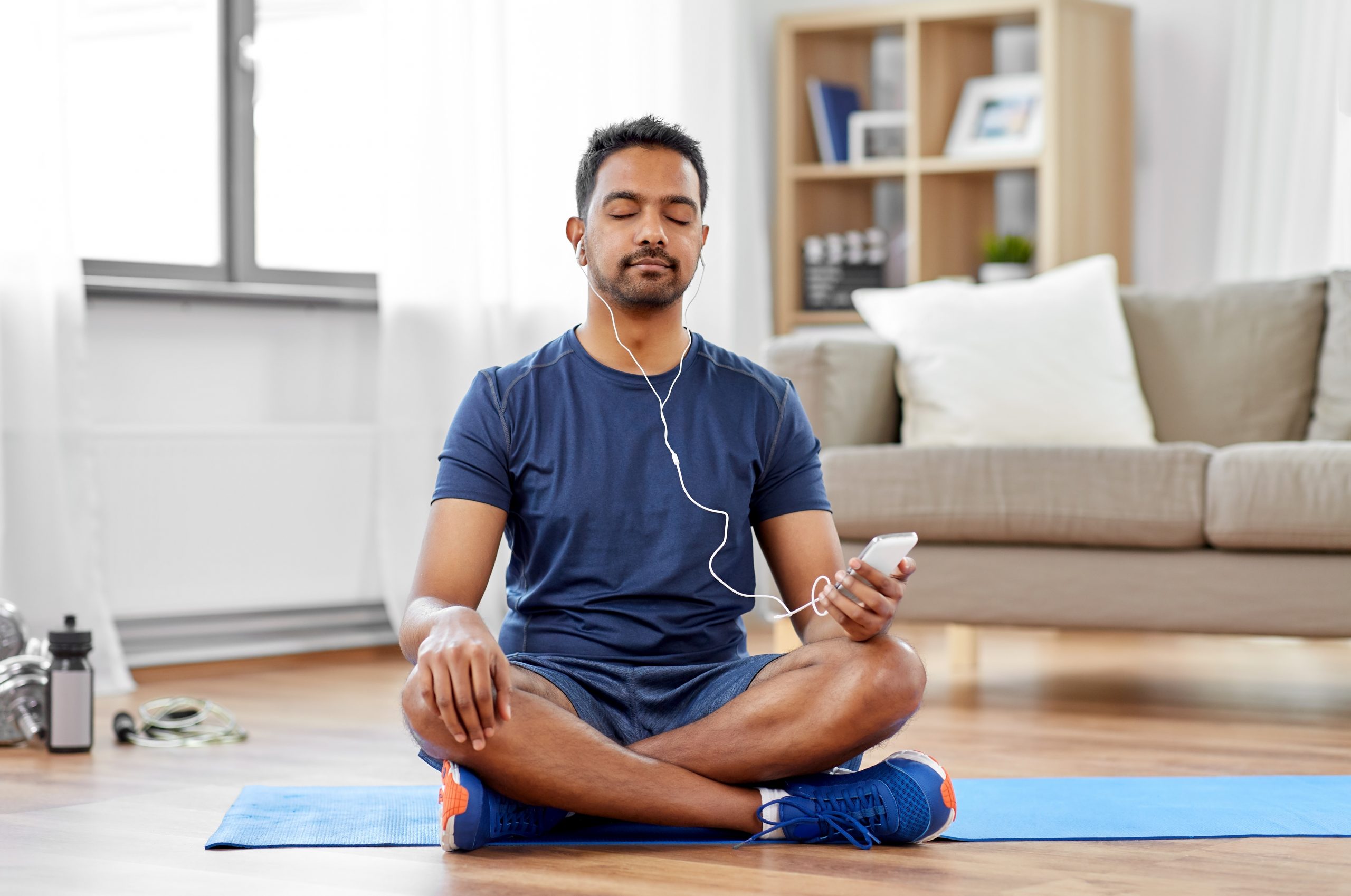 indian man with smartphone on exercise mat at home