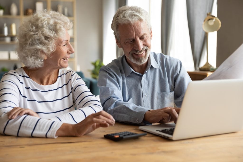 Elderly couple sitting at table using laptop and online banking feels satisfied checking utility bills or financial statement papers, easy access, reading good news received letter from bank concept