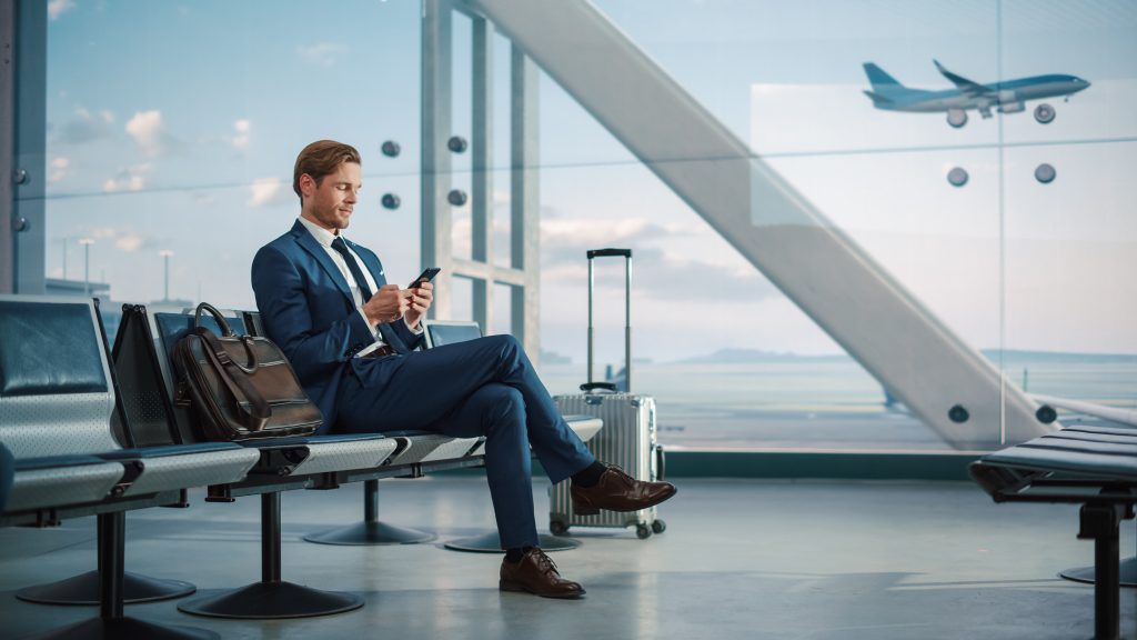 Airport Terminal: Businessman Uses Smartphone, Waiting for a Fli