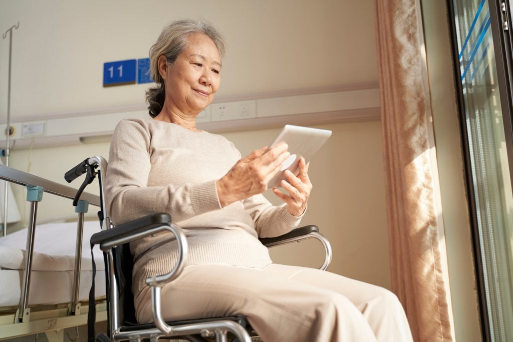 asian senior woman using digital tablet in nursing home or hospital ward