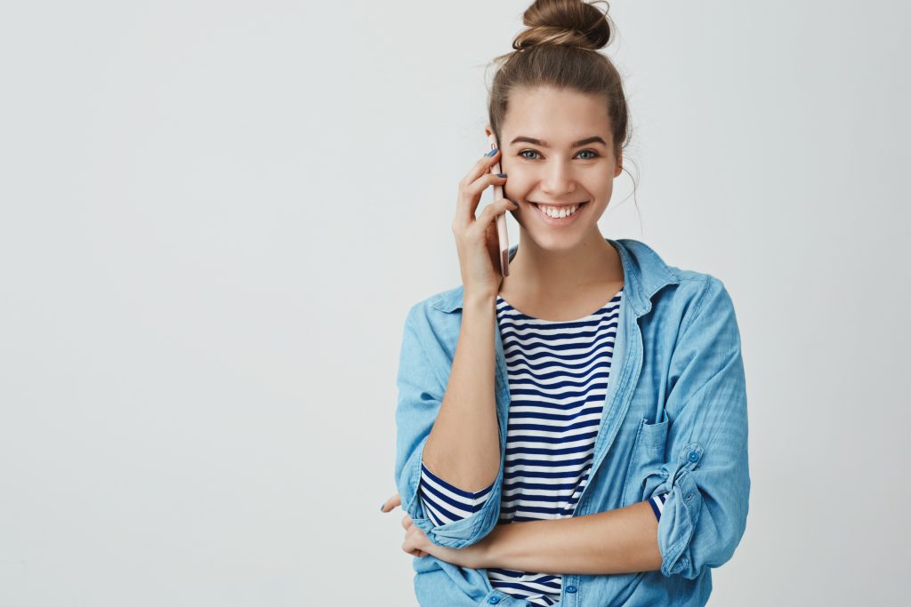 Happy excited attractive young woman calling friend spending free-time home gossiping discussing last fashion trends smiling broadly feeling joyful amused, holding smartphone, white background.
