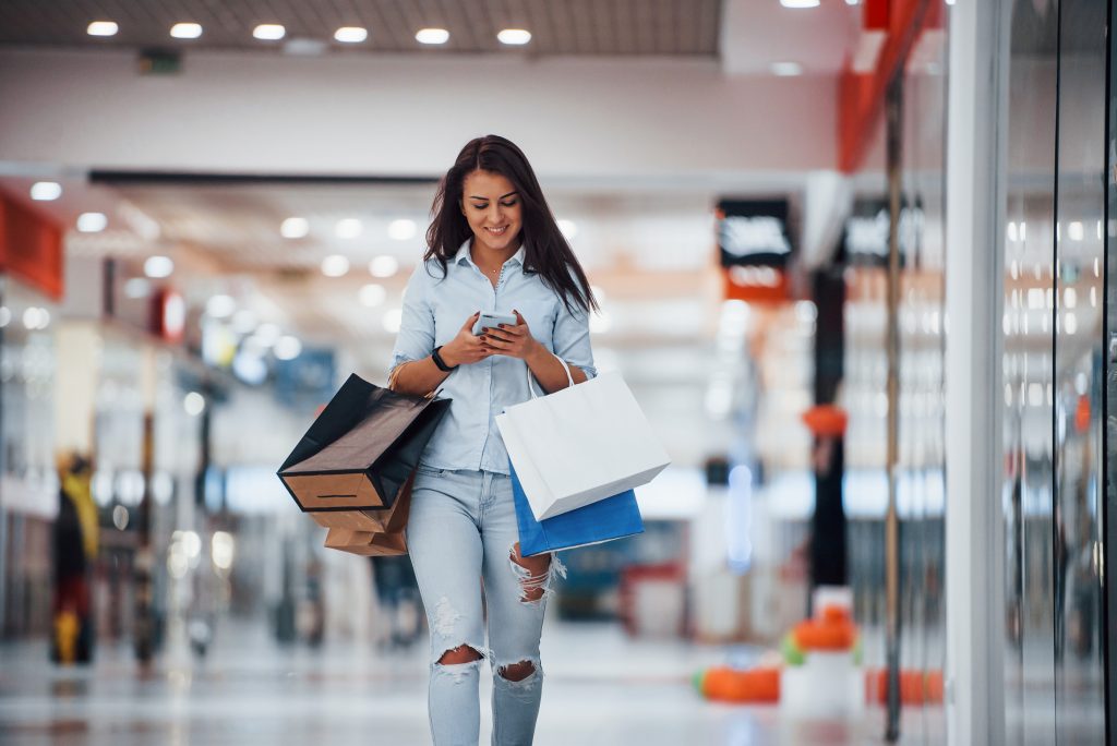 Brunette woman in the supermarket with many of packages and phone in hands have shopping day.