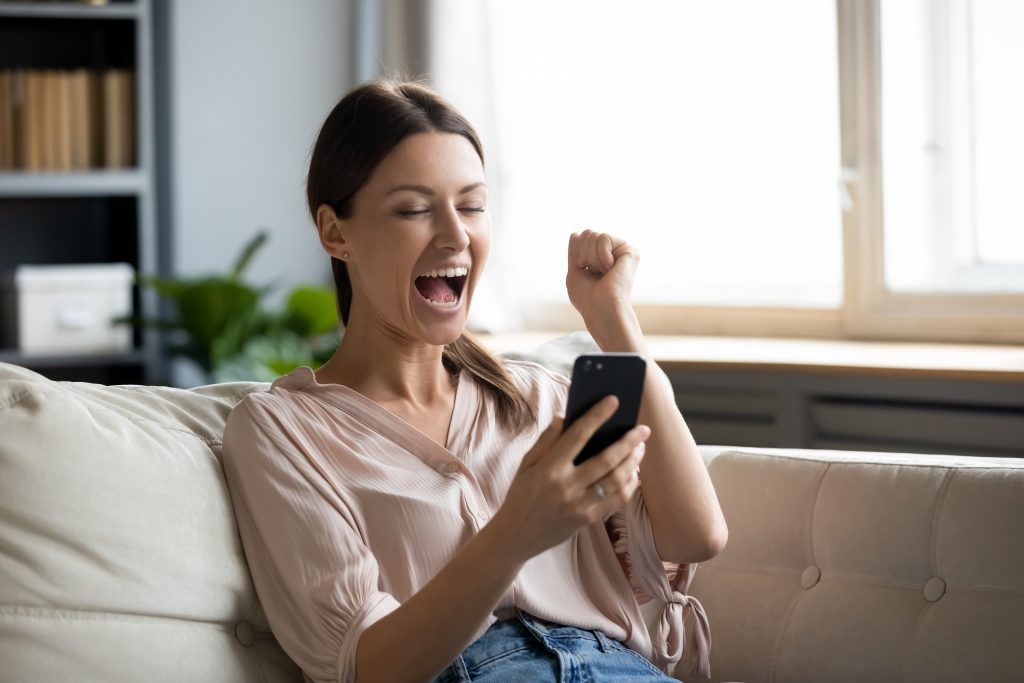 Close up overjoyed woman holding phone, screaming with joy, showing yes gesture, excited young female celebrating success, online lottery win, reading good news in email, using smartphone