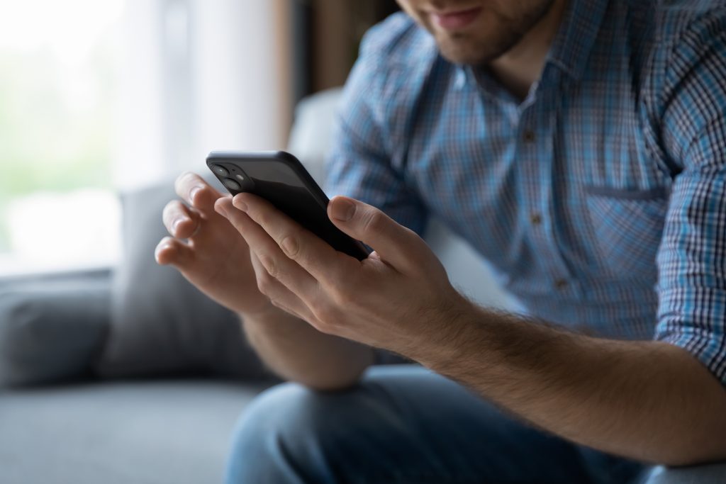 Hands of man using online virtual app on mobile phone. Millennial guy chatting on smartphone, using banking services, reading text message, typing, shopping, making call, browsing internet. Close up