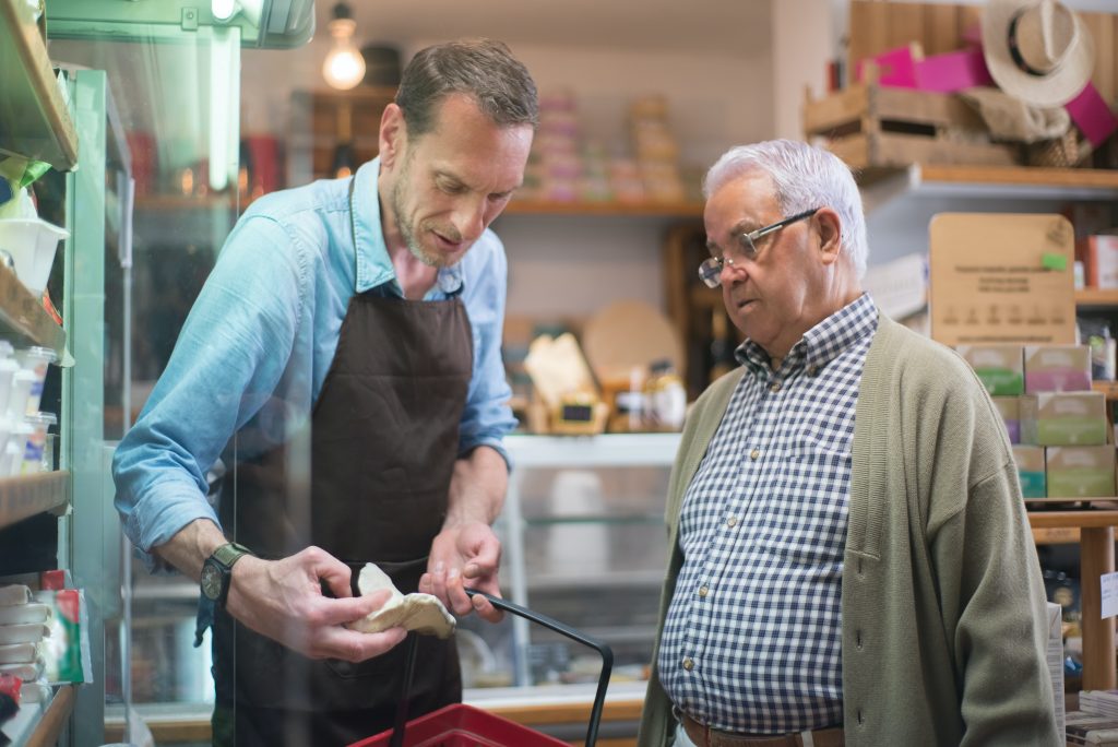 Attendant helping an old man to choose products in a groery store