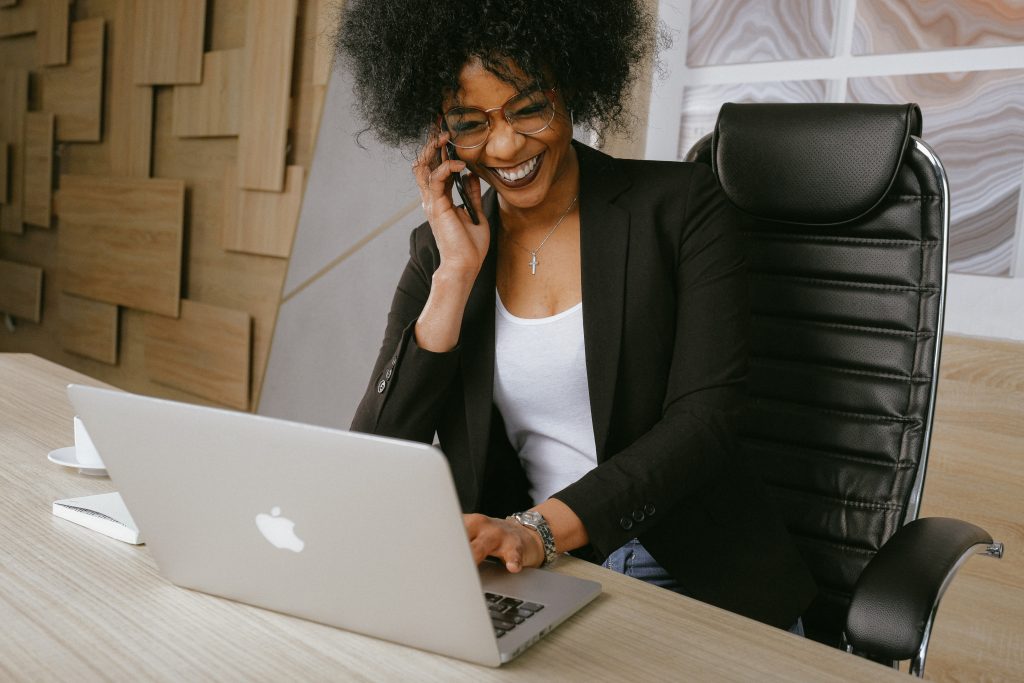 Black woman smiling during a phone call while uses her laptop