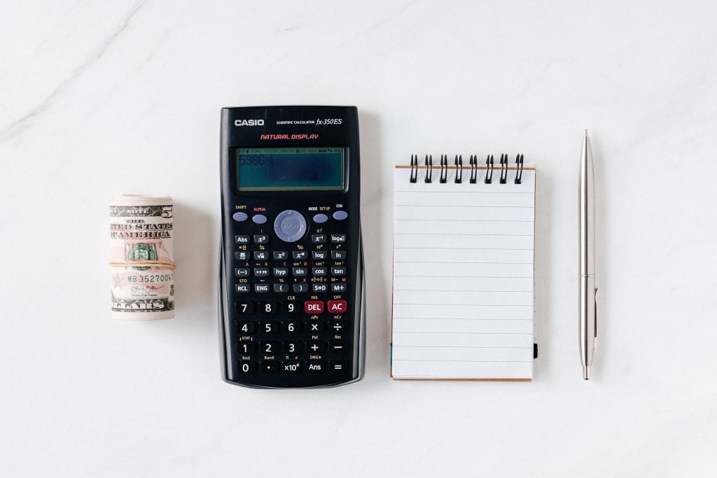 top view of a calculator, notebook, pencil and cash on a white background