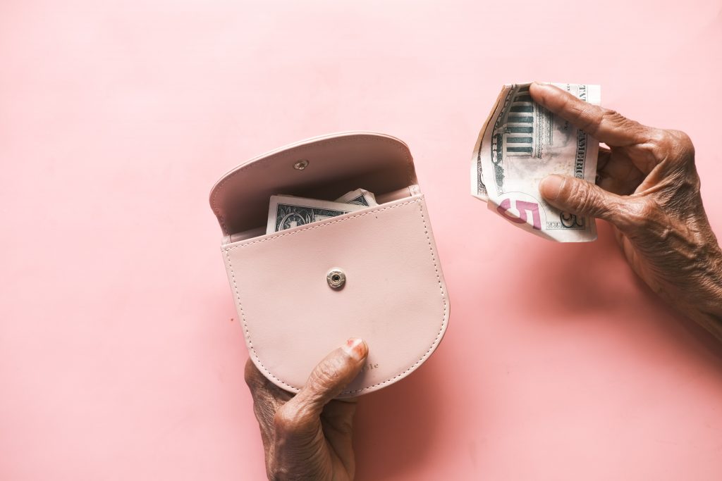 Female hand holding a pink wallet and some cash