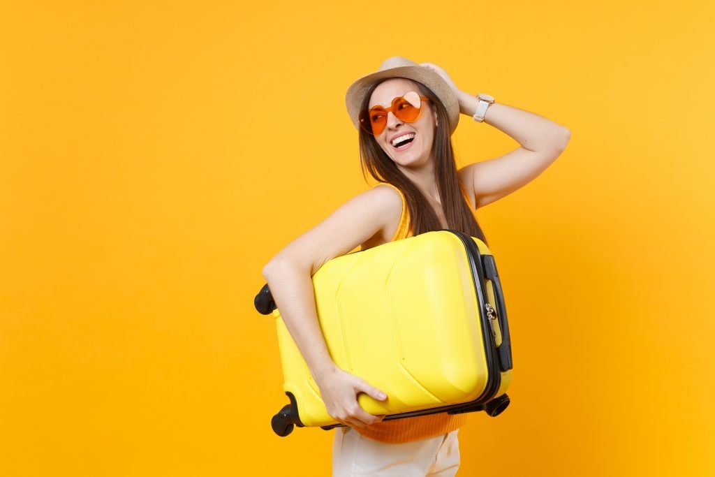 Traveler tourist woman in summer casual clothes, hat with suitcase isolated on yellow orange background. Female passenger traveling abroad to travel on weekends getaway. Air flight journey concept