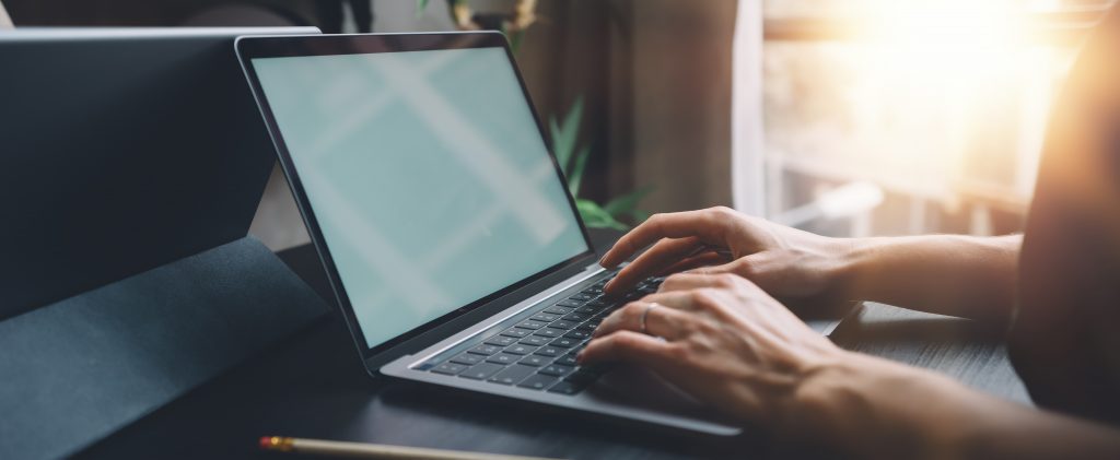 Female hands typing on laptop keyboard at the office. Wide