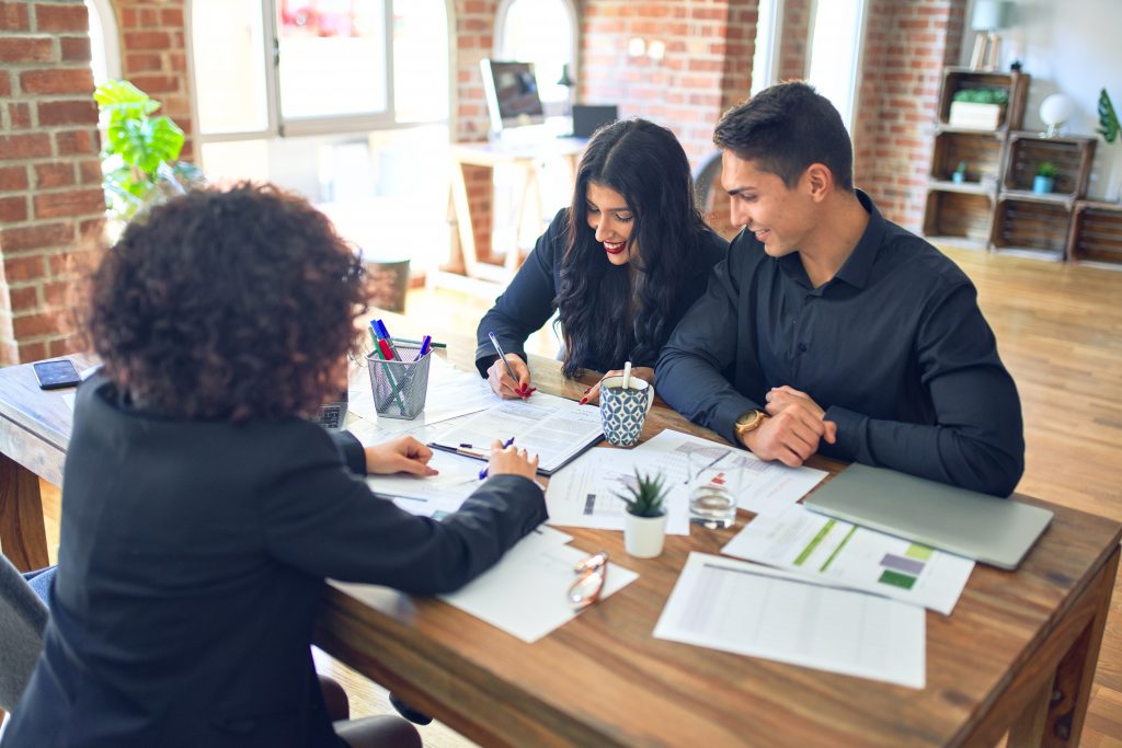 Young beautiful couple applying for mortgage. Sitting smiling happy meeting with real state agent signing mortgage loan at bank