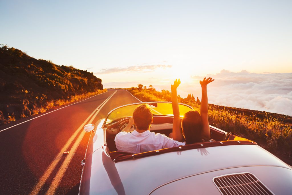 Happy Couple Driving on Country Road into the Sunset in Classic Vintage Sports Car