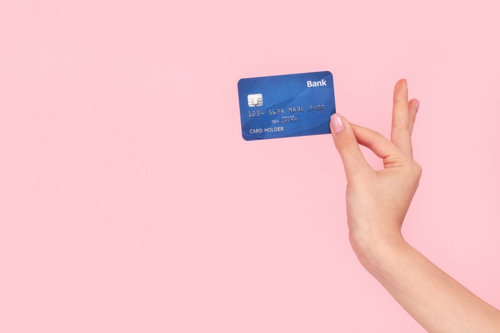 Crop hand of woman holding blue credit card on pink background