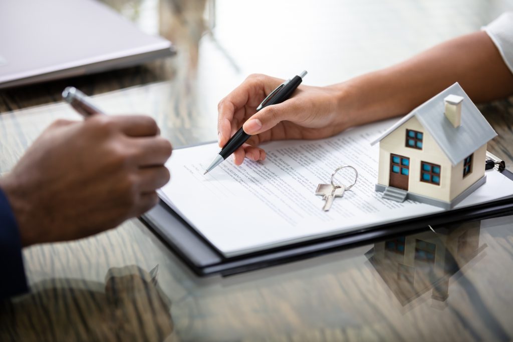 Businessman Signing Real Estate Contract With Keys On It