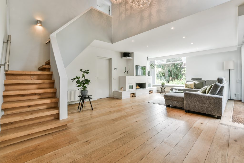 A cozy house interior with a wooden floor, large gray sofa, and stairs leading to the second floor