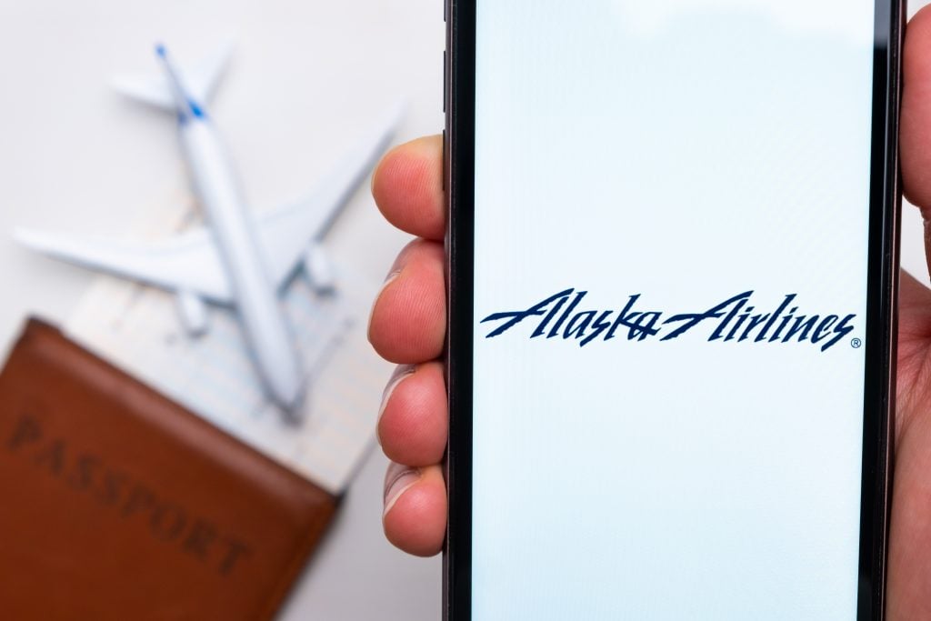 Alaska Airlines airlines company app or logo displayed on a mobile phone with passport, boarding pass and plane on the background, September 2021, San Francisco, USA