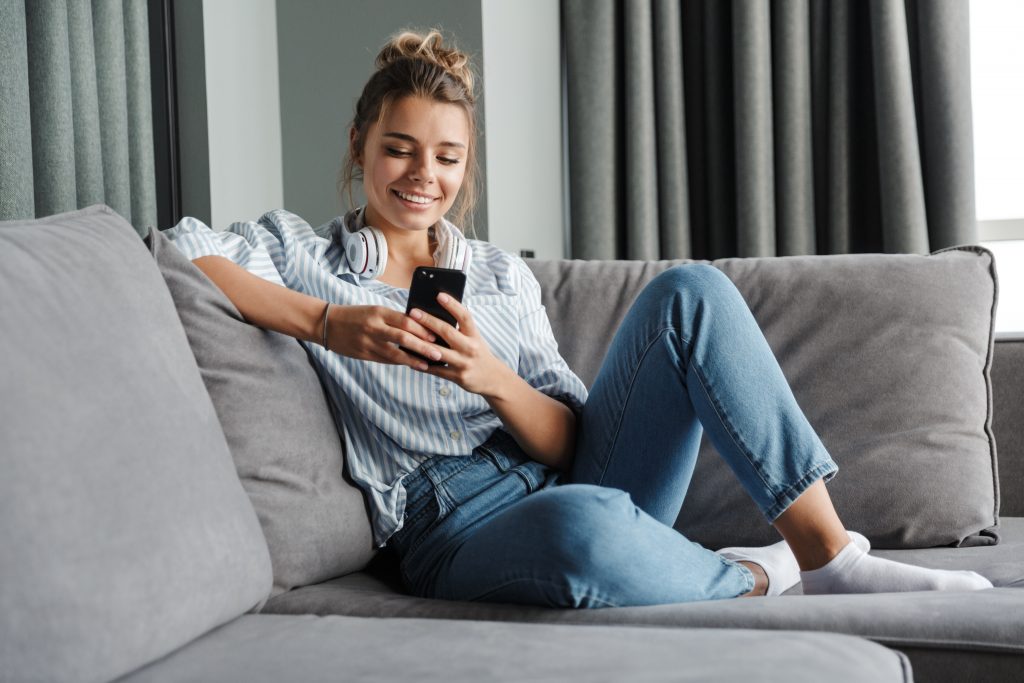 Image of smiling nice woman using cellphone while sitting on sof