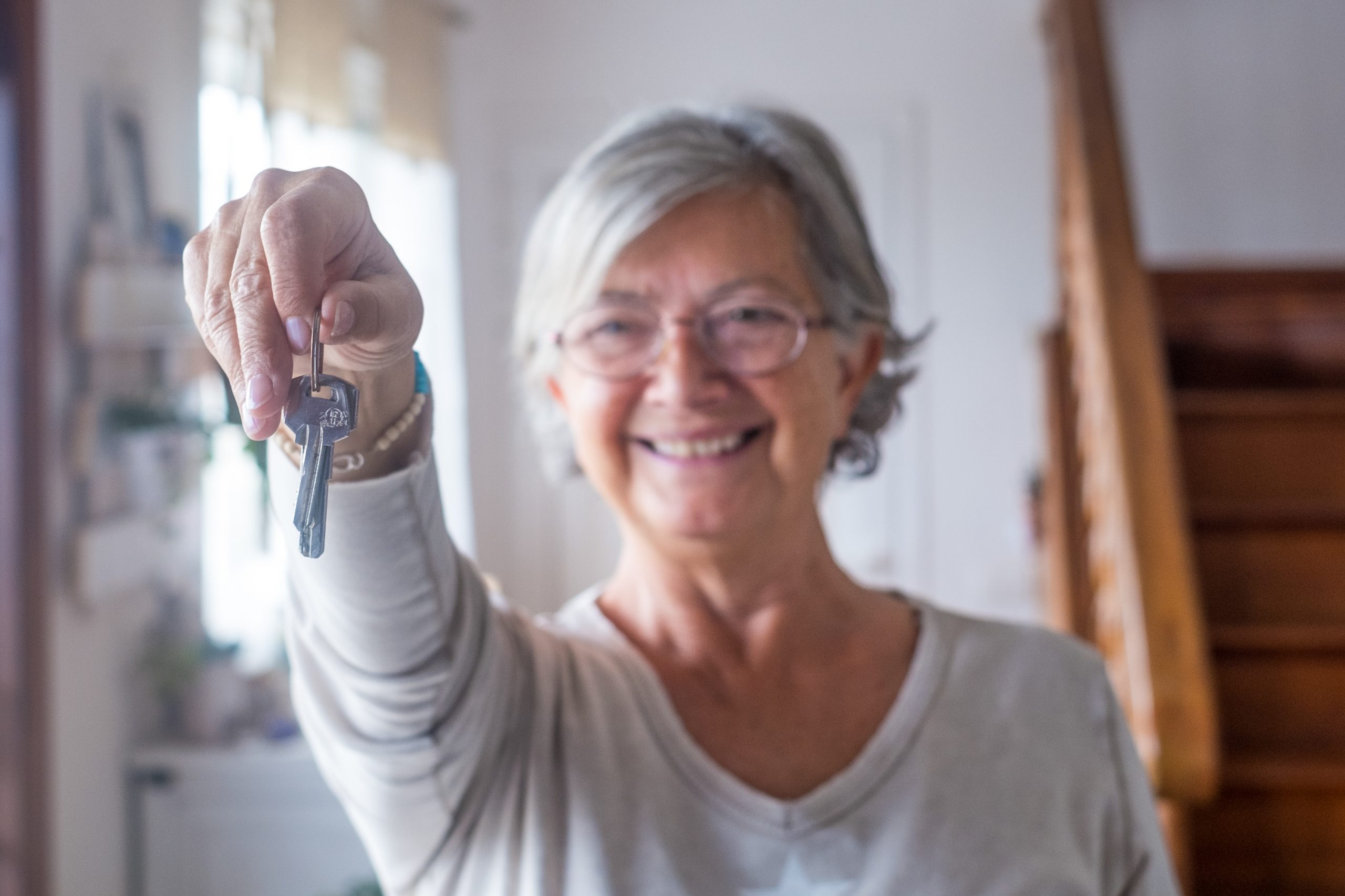 Close up of old and mature woman at home holding keys of house t