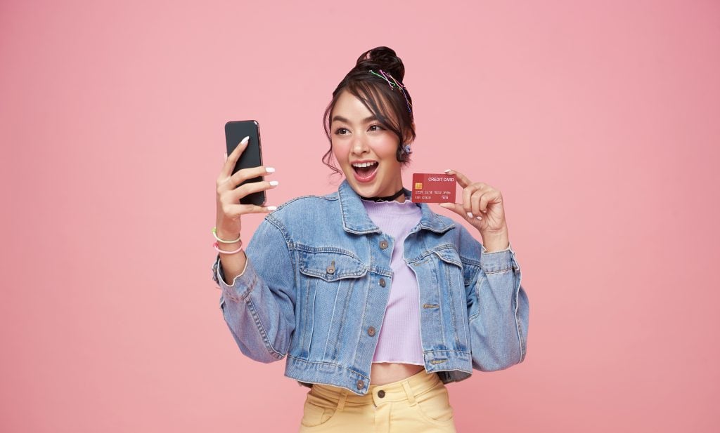 happy young asian woman using mobile phone and credit card isola