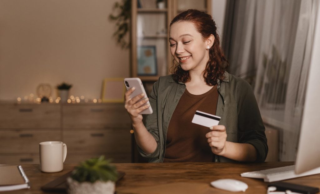 smiley-woman-using-her-smartphone-home-with-credit-card