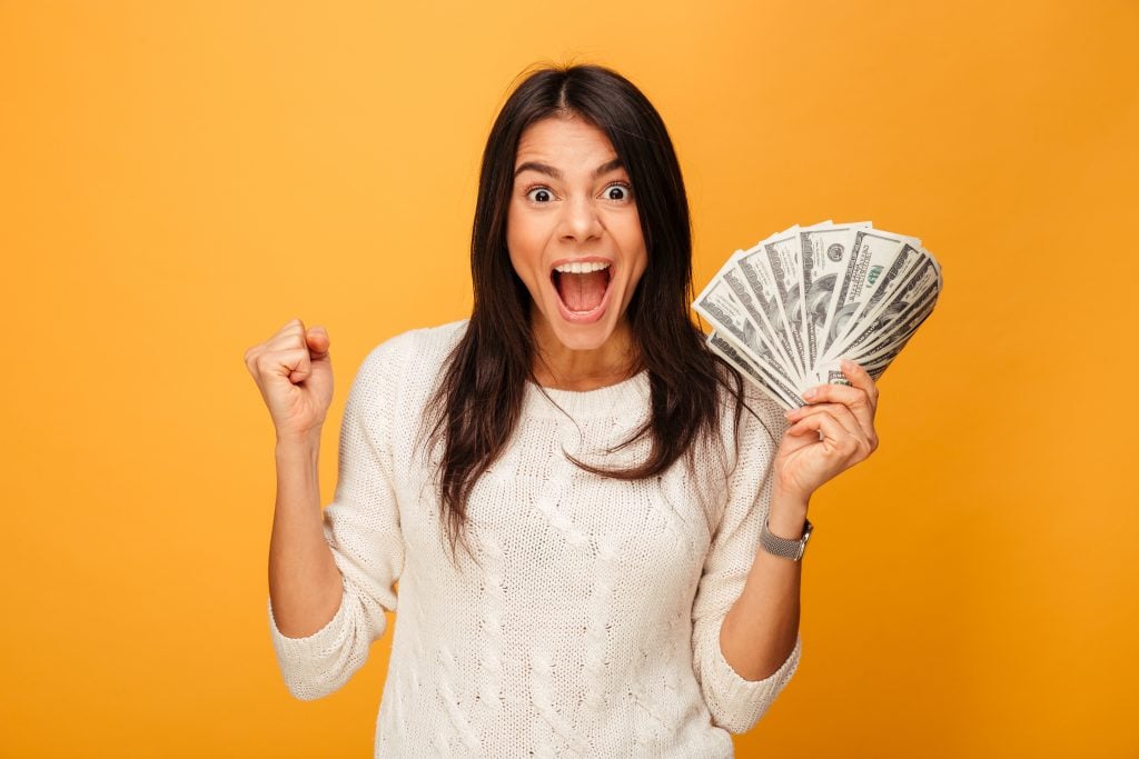 Portrait of an excited young woman holding money banknotes