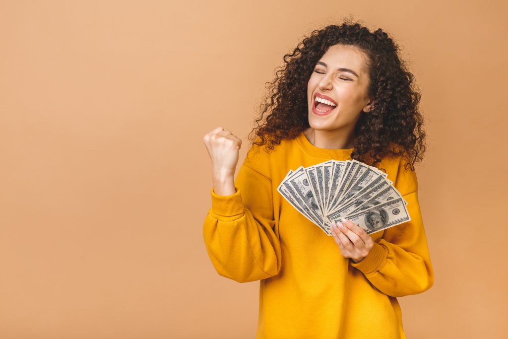 Portrait of a cheerful young woman holding money banknotes and c