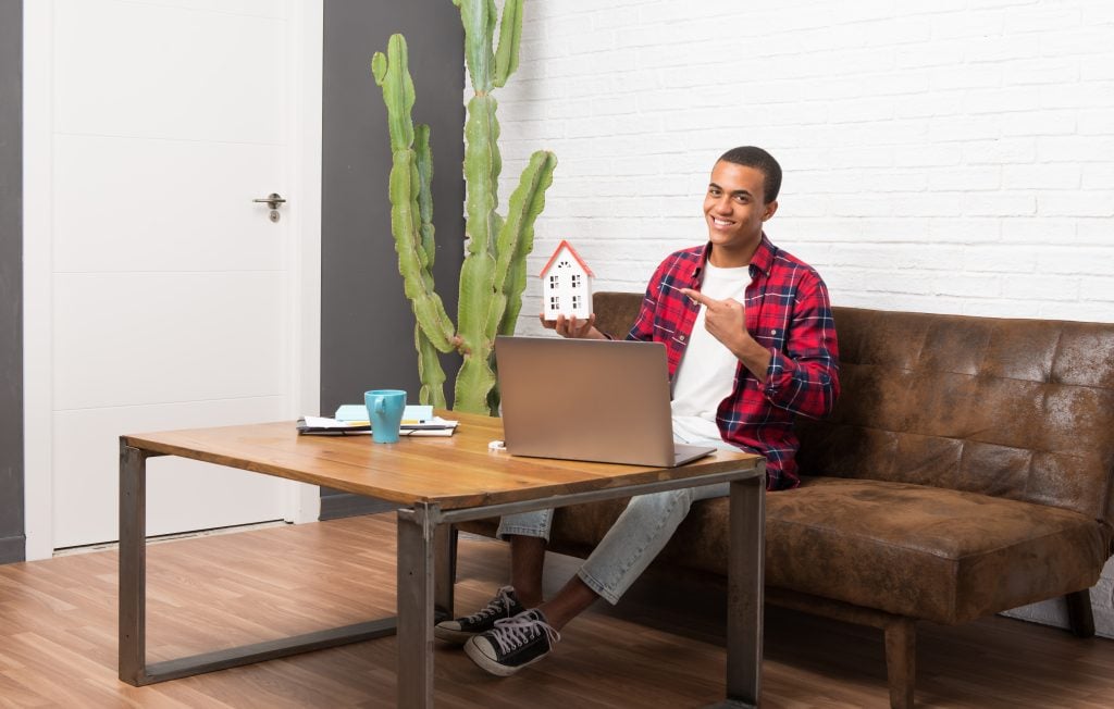 African american man with laptop in the living room holding a li
