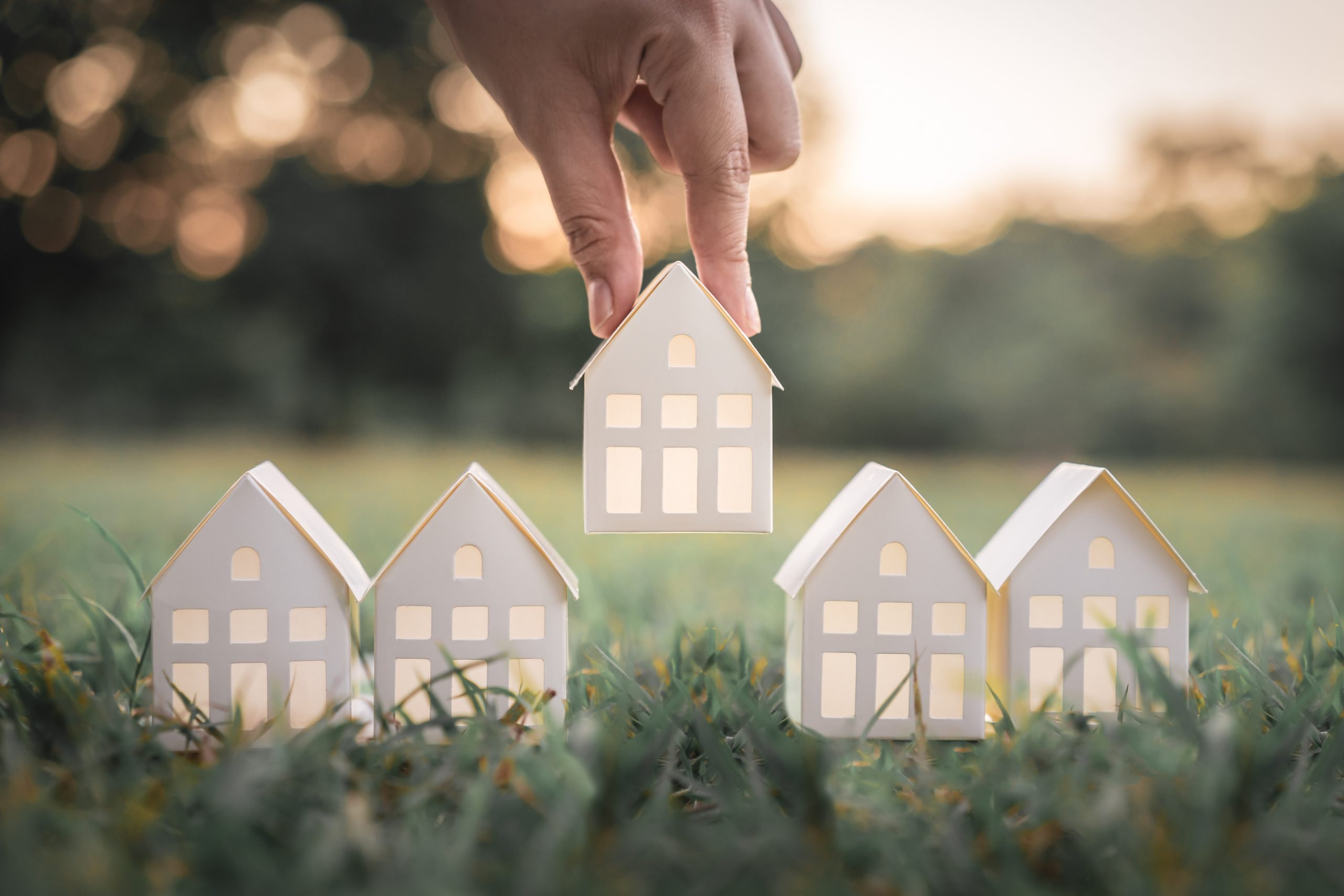 hand-choosing-white-paper-house-model-from-group-house-green-grass