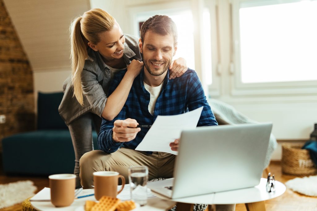 Happy couple analyzing their home budget while paying bill on a computer.