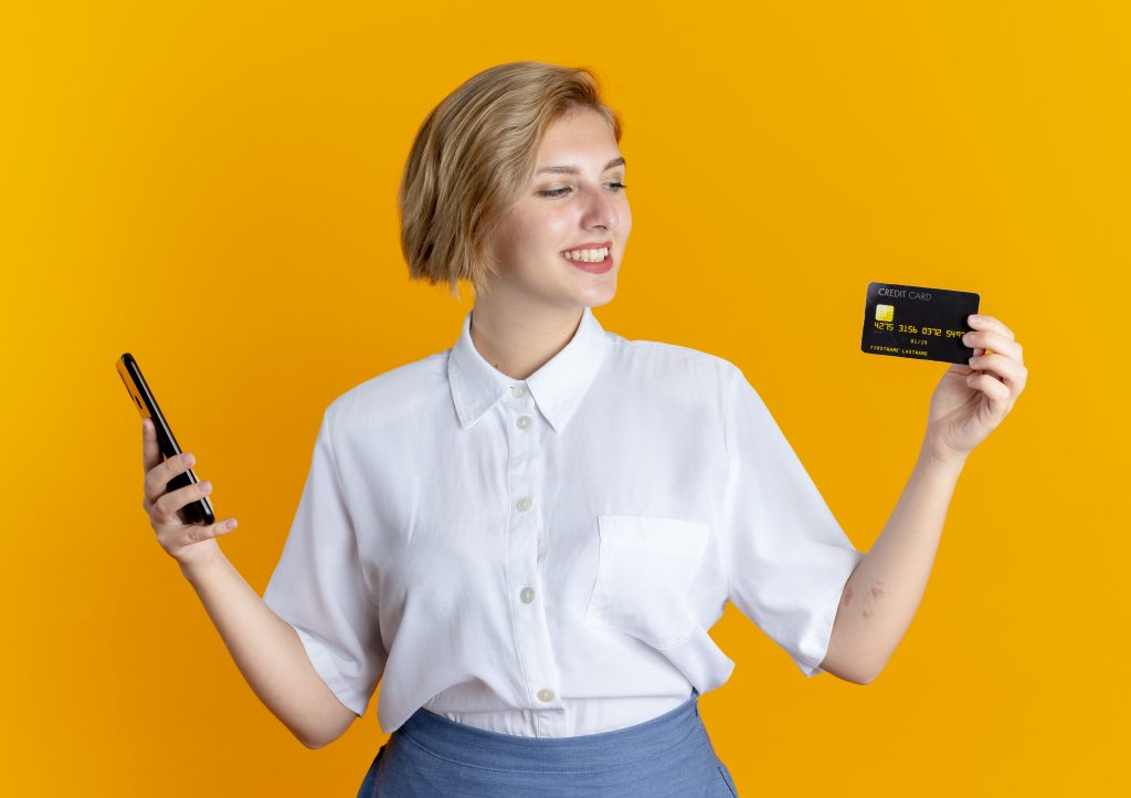 young-smiling-blonde-russian-girl-holds-phone-looks-credit-card