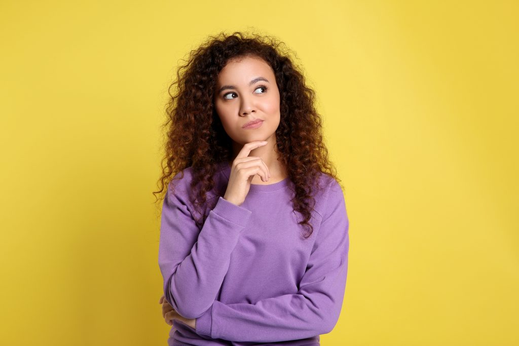 Pensive African-American woman on yellow background. Thinking ab