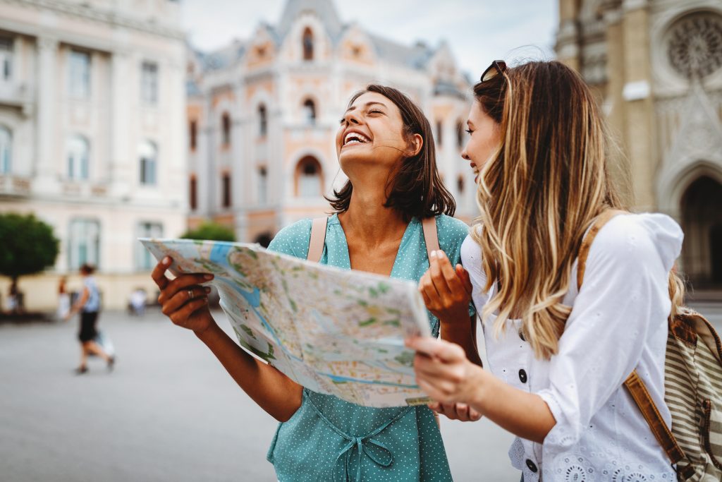 Fun, friends, travel and tourism concept. Beautiful girls looking for direction in the city