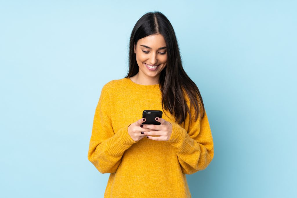 Young caucasian woman isolated on blue background sending a message with the mobile