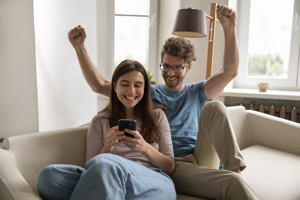 Excited surprised successful young couple using mobile phone together