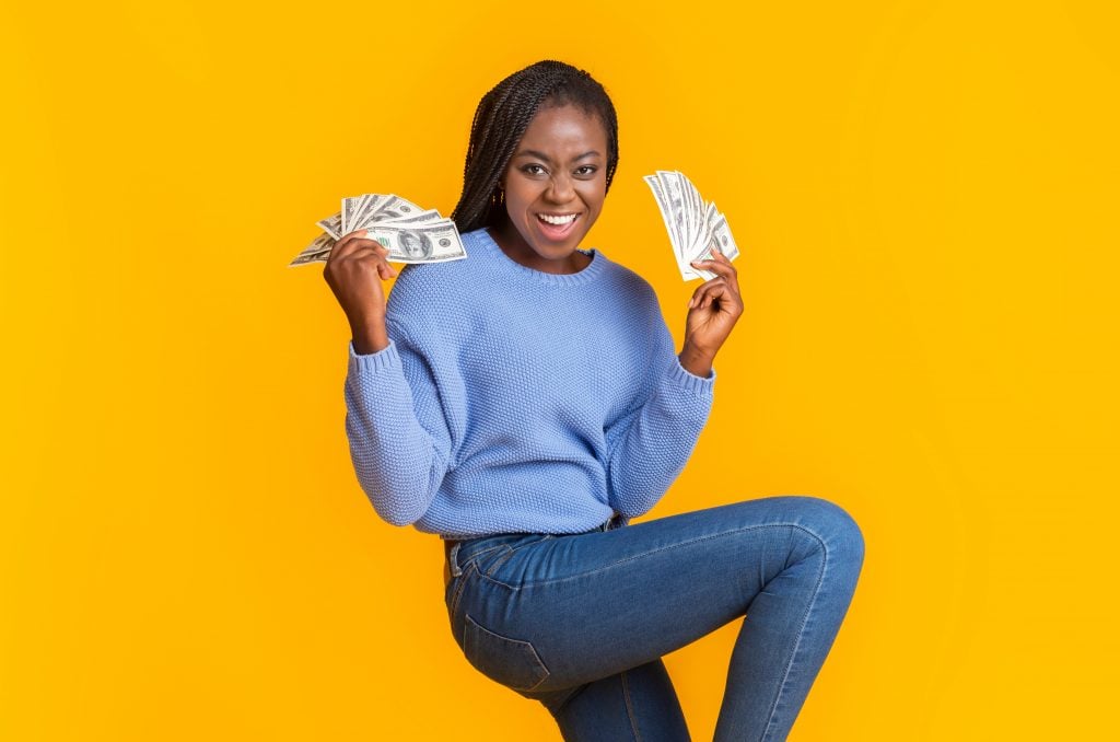 Extremely happy young black woman holding money in both hands
