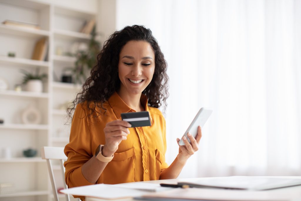 Happy woman using a credit card while holding a phone