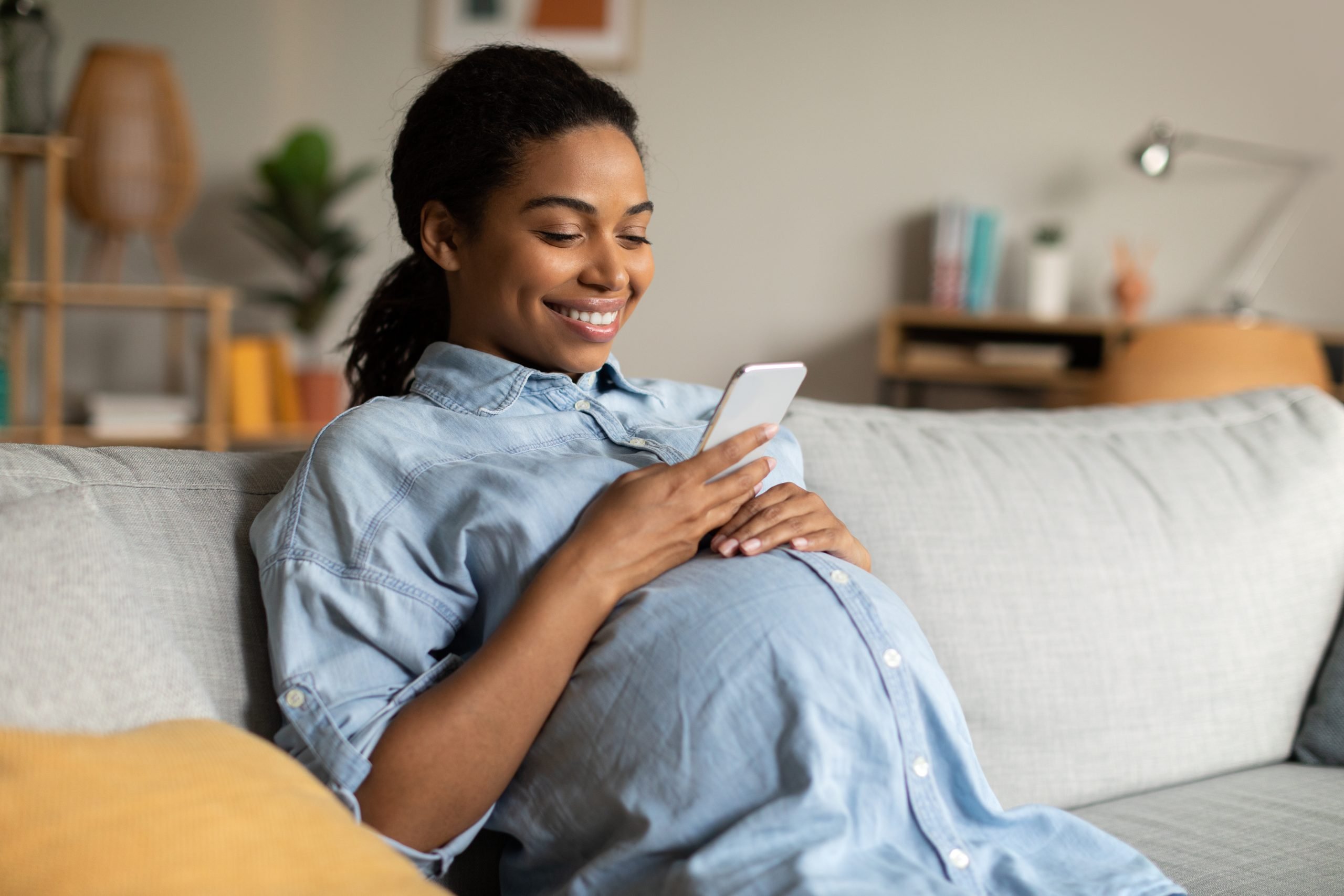 Pregnant African Woman Using Mobile Phone Texting Sitting At Home