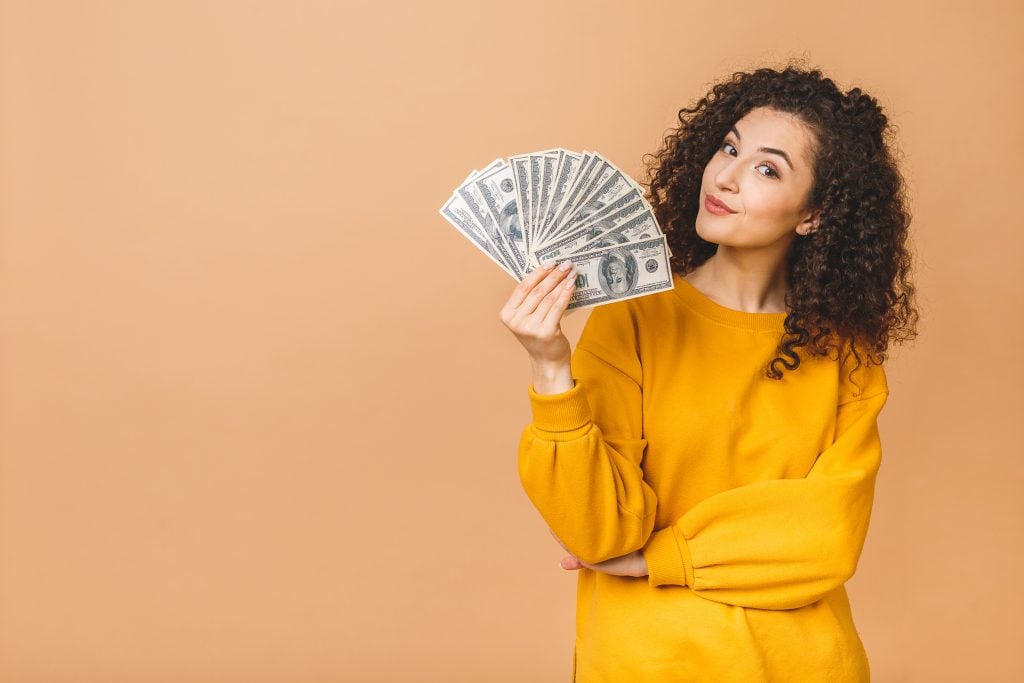 Portrait of a cheerful young woman holding money banknotes and c
