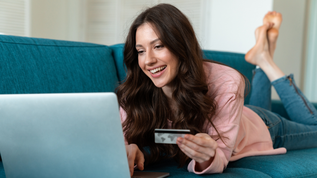 woman smiling at her laptop while holding a credit card