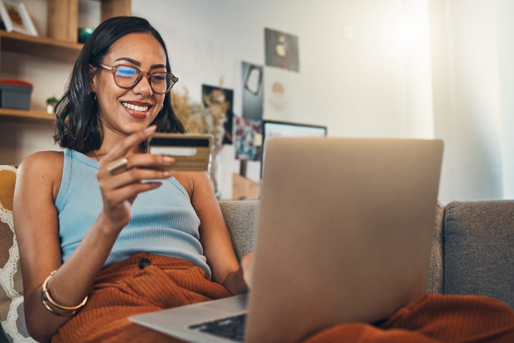 Woman on couch with laptop, credit card and online shopping, payment and ecommerce with fintech at home. Happy female customer at apartment, bank app and sale on store website with internet banking