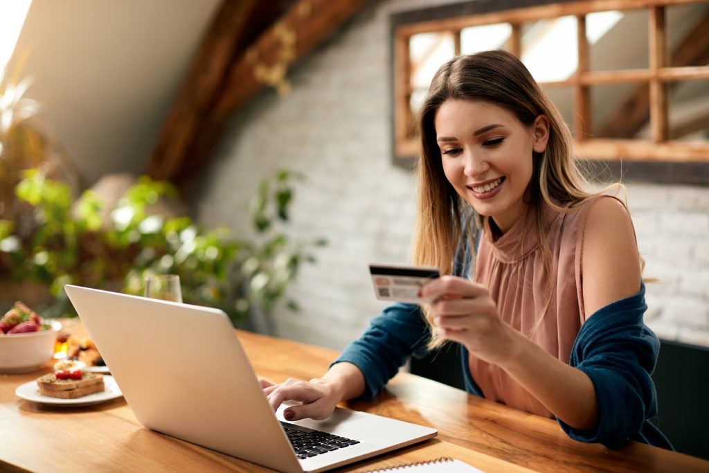 Young happy woman using computer and credit card while shopping on the Internet at home.